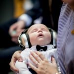 A cute baby wearing headphones and a bow tie sleeping peacefully in an indoor setting.