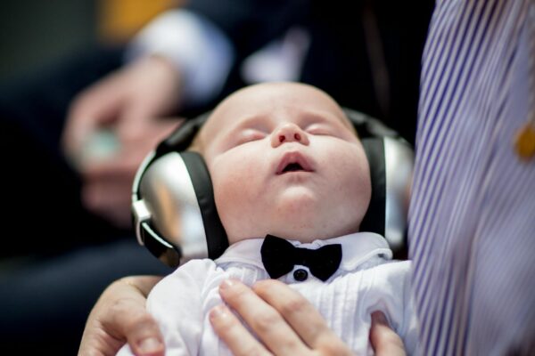 A cute baby wearing headphones and a bow tie sleeping peacefully in an indoor setting.