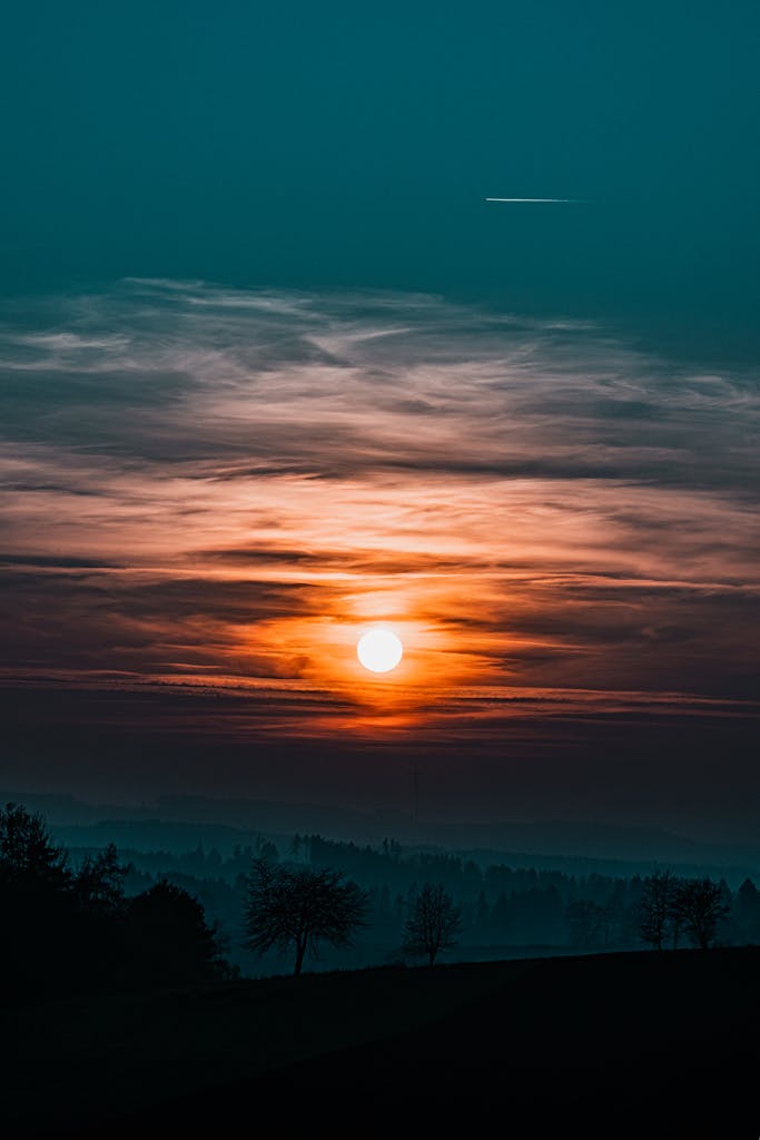 A stunning sunset scene with silhouetted trees and vibrant cloud patterns in the sky. ग्रहण क्या होता है 