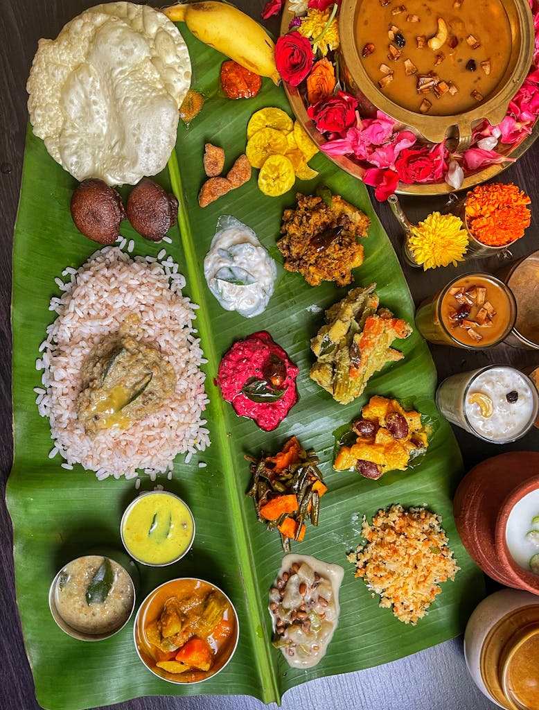 An elaborate South Indian meal with various dishes artfully arranged on a banana leaf, showcasing vibrant colors and textures. Onam 2025