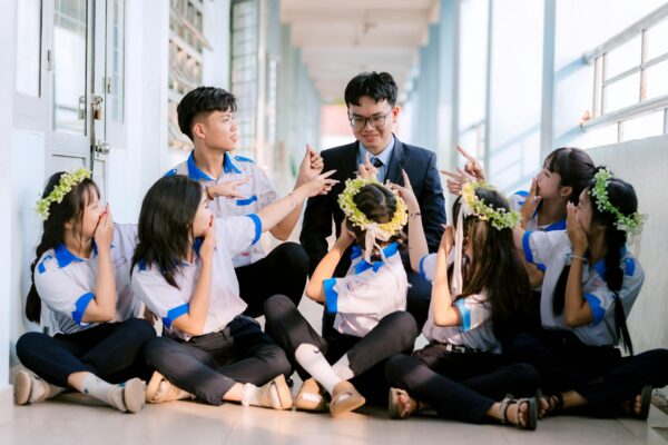 Group of happy students in uniform celebrating with their teacher in a hallway.